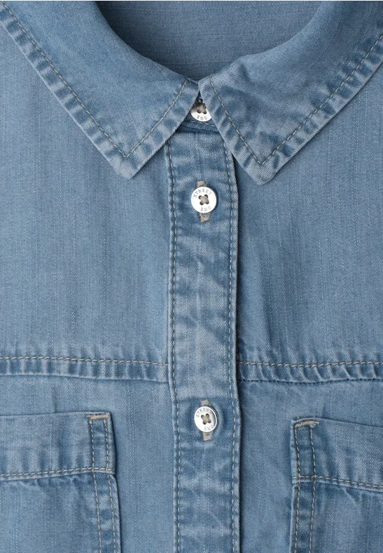 Close-up van een blauwe spijkerjas met metalen knopen en borstzakken.