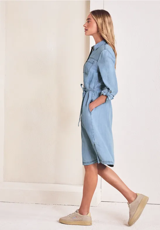 Zijaanzicht van een vrouw in een lichtblauwe denim jumpsuit met ceintuur en plateauzolen.