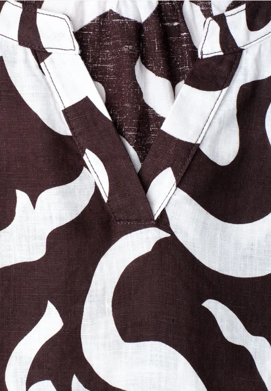 Close-up van donkerbruin textiel met witte, vloeiende patronen en een V-hals.