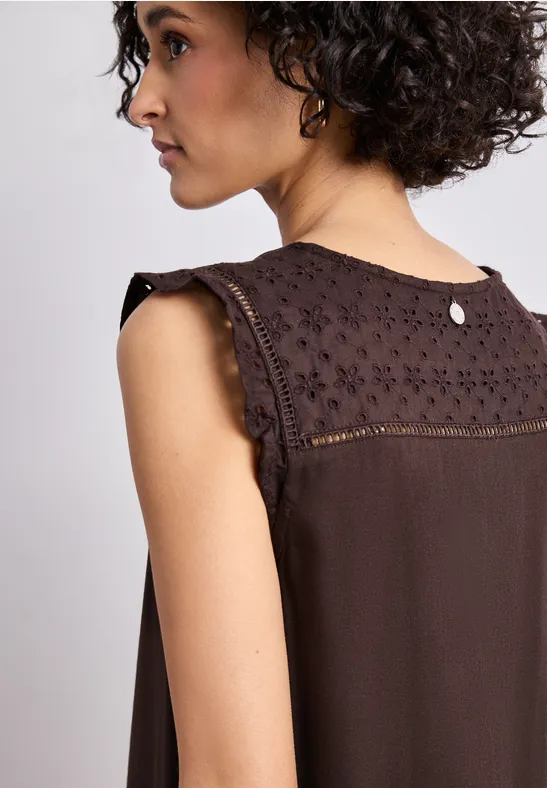 Frau im Profil trägt ein ärmelloses, braunes Top mit Spitzenbesatz auf den Schultern.