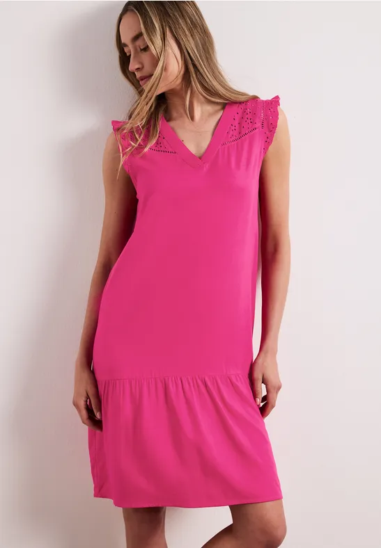 Vrouw in knielange mouwloze fuchsiaroze jurk met kant op de schouders voor een witte achtergrond