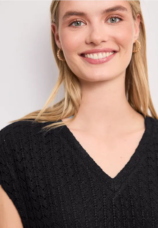 Een vrouw met lang blond haar draagt een zwarte V-hals trui.