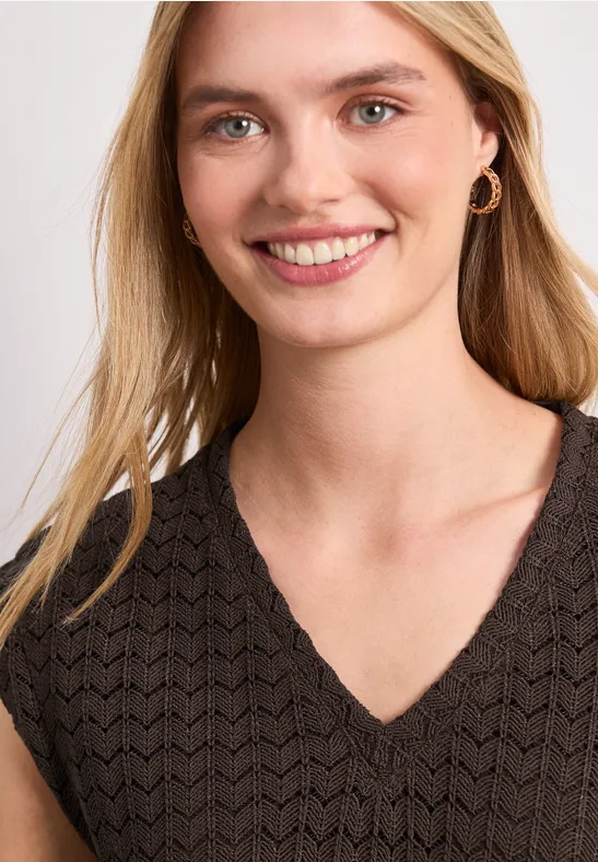 Vrouw met blond haar, gouden oorbellen, draagt een zwarte, gestructureerde V-hals top.