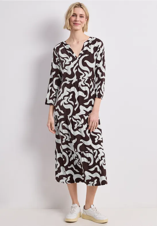 Vrouw in een midijurk met abstracte zwart-witte print en witte sneakers.