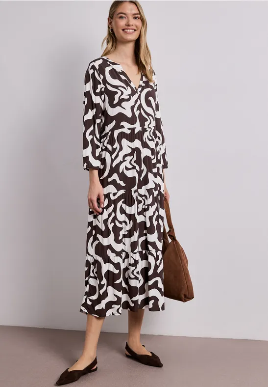 Vrouw in middenlange, zwart-witte jurk met V-hals, zwarte platte schoenen en bruine tas.
