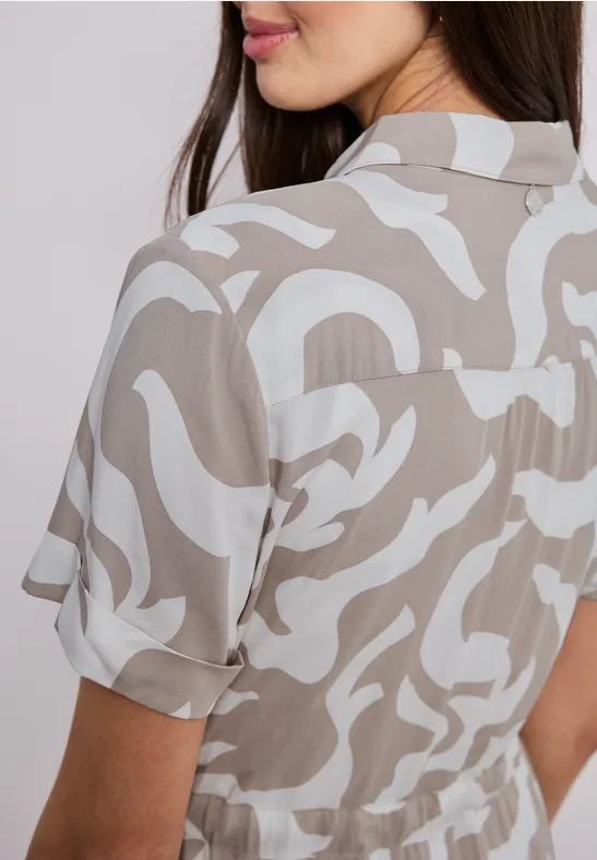 Rückansicht einer Frau in beige-weiß gemustertem, kurzärmeligem Hemd.