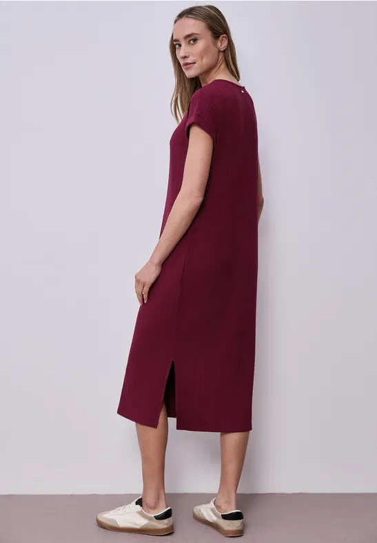 Frau trägt lässiges midikurzes, burgunderfarbenes T-Shirt-Kleid mit Seitenschlitzen und weißen Sneakern.
