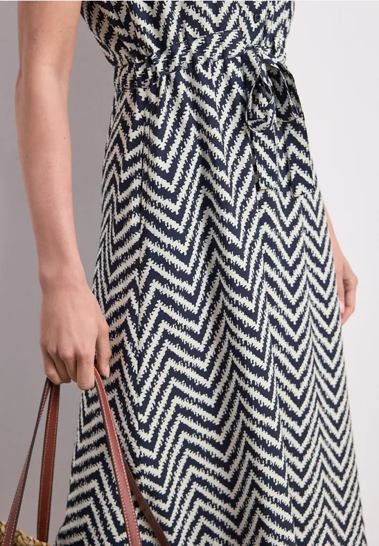 Zwart-witte midi-jurk met zigzagprint en tailleceintuur, vastgehouden aan een tasband.