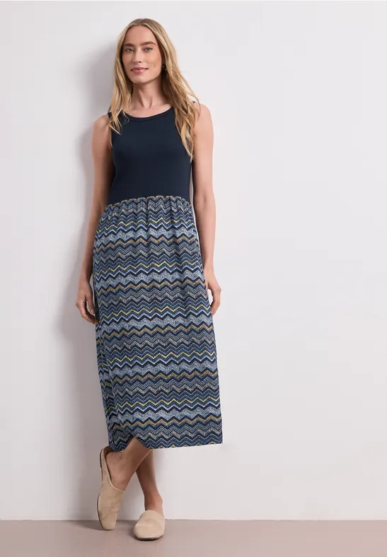 Vrouw in mouwloze maxi-jurk met marineblauw bovenstuk en multicolor zigzag rok.