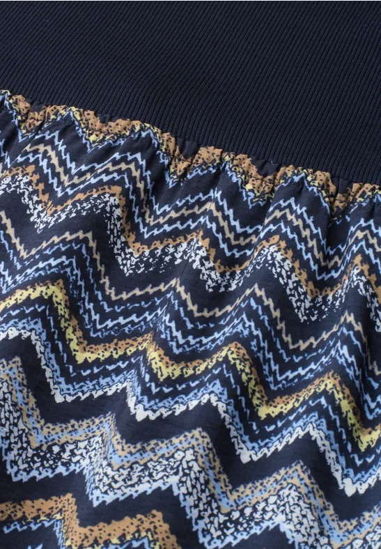 Gebreide stof met golvend zigzagpatroon in blauw, wit, geel en bruin, bovenrand donkerblauw.
