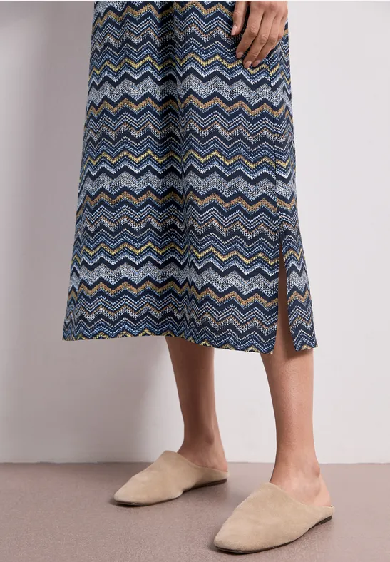 Een midirok met kleurrijk zigzagpatroon en een zijsplit, gecombineerd met beige slippers.