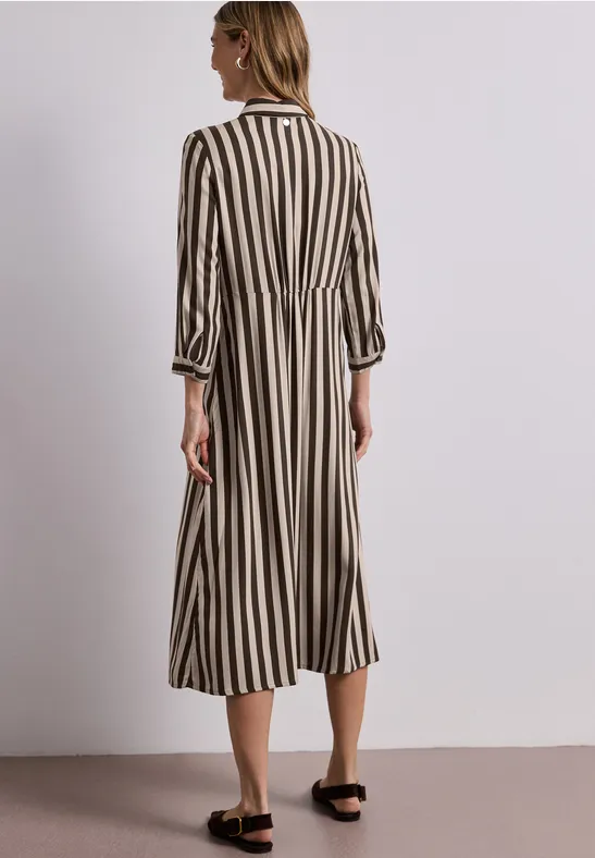 Vrouw van achteren in een lange jurk met verticale strepen en zwarte sandalen.