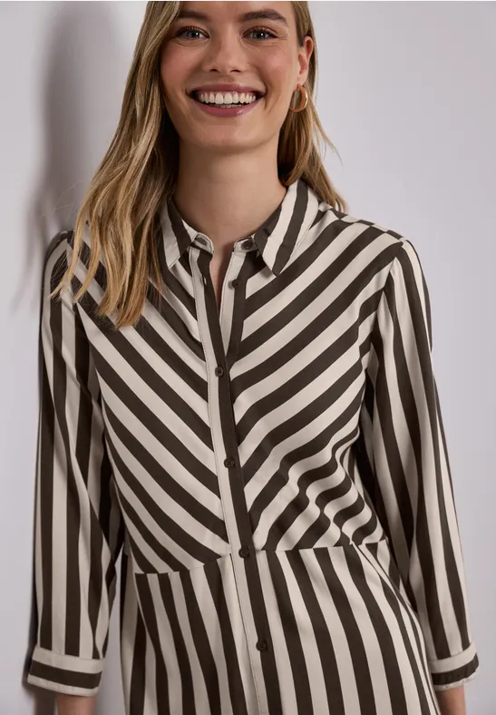 Een vrouw draagt een blouse met diagonale zwart-beige strepen.