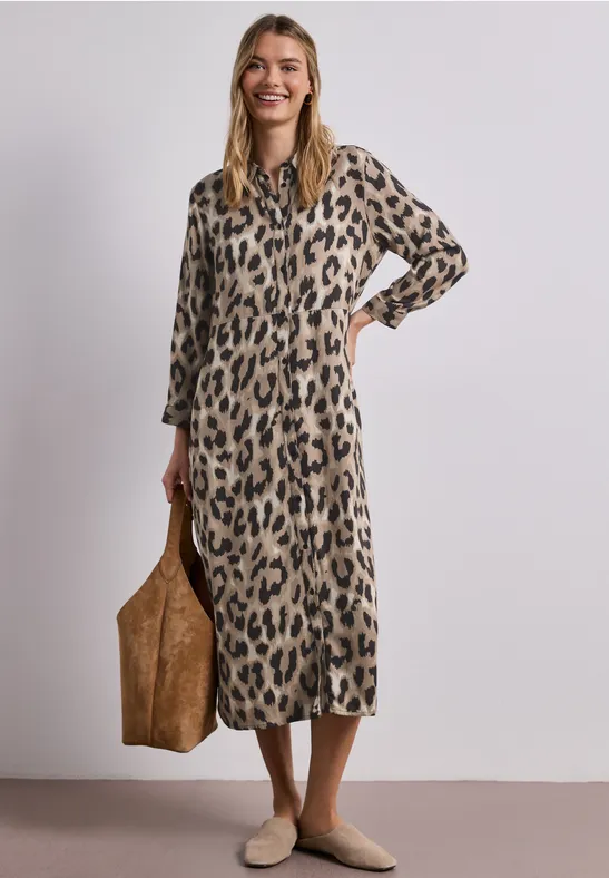 Frau in knöchellangem Leopardenkleid trägt große braune Tasche und beige Schuhe.