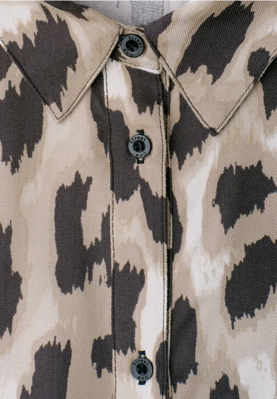 Nahaufnahme eines beige-braunen Hemds mit animalischem Fleckenmuster und schwarzen Knöpfen.
