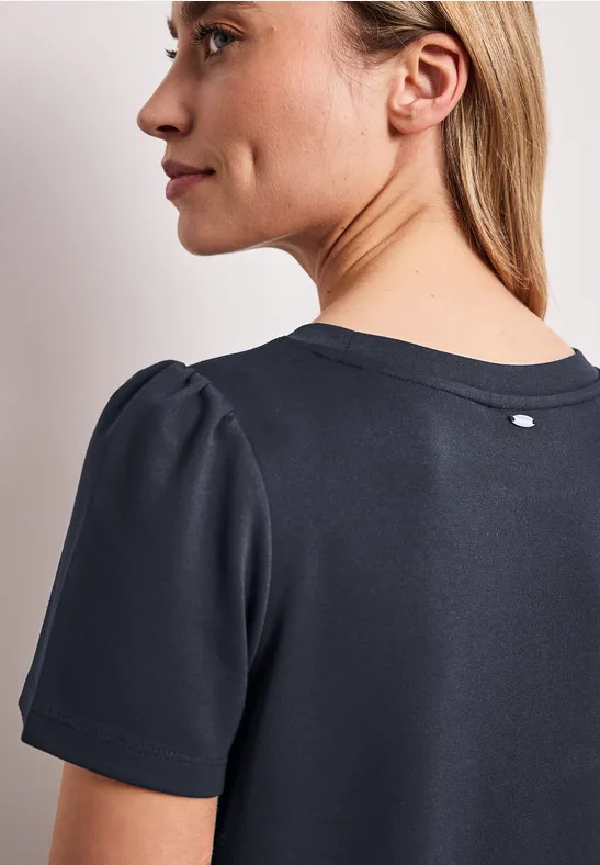 Zijaanzicht van een vrouw in een donkerblauw T-shirt met licht opgepofte mouwen