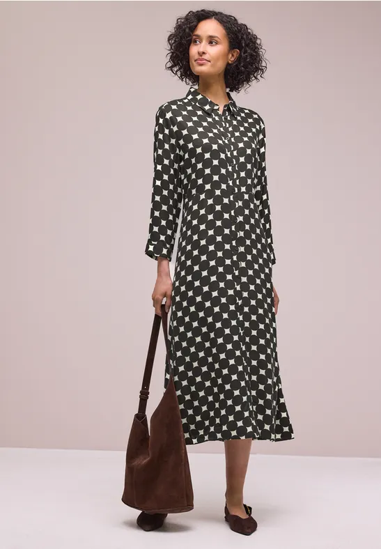 Frau in Midi-Hemdkleid mit weißem Sternmuster, brauner Wildleder-Tasche und braunen Mules.