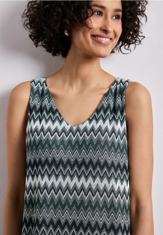 Persoon met krullend haar draagt een mouwloze V-hals top met grijs-wit-zwart zigzagpatroon.