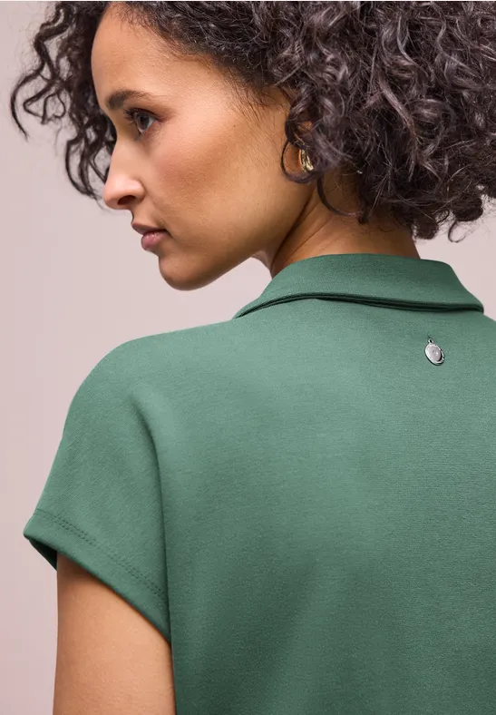 Vue de dos d'une personne aux cheveux bouclés portant un polo vert.