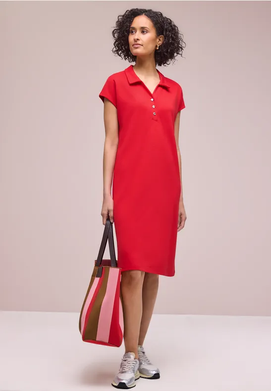 Femme en robe polo rouge, baskets argentées et sac à bandoulière rayé.