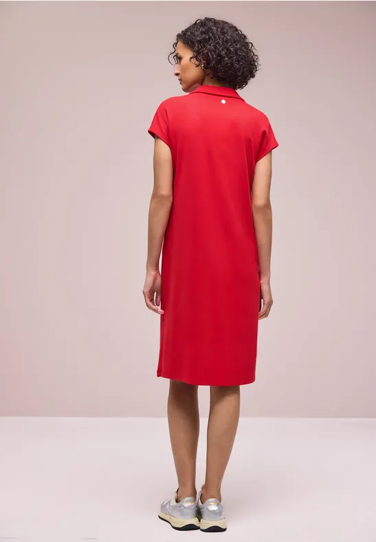 Femme de dos portant une robe polo rouge et des baskets sur fond neutre.