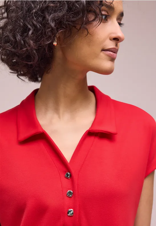 Personne aux cheveux bouclés portant un polo rouge.