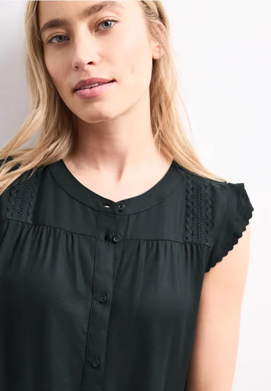 Vrouw draagt mouwloze zwarte top met kantdetails op de schouders.