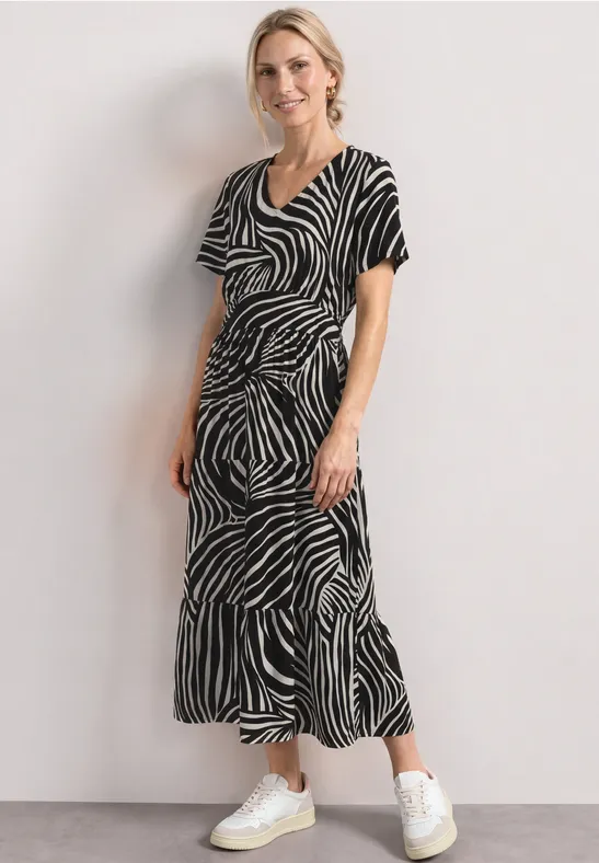 Vrouw in zwart-witte zebrajurk en witte sneakers tegen een lichte achtergrond.