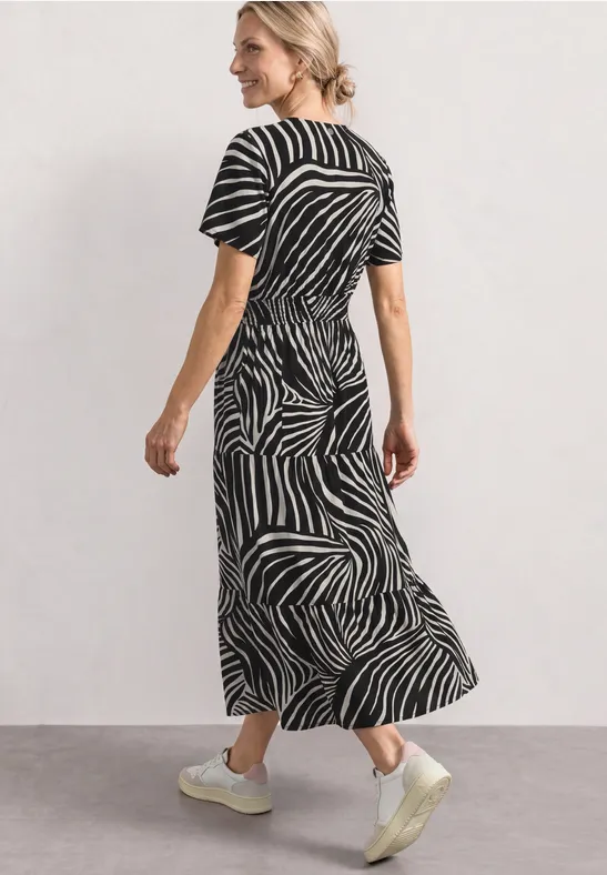 Vrouw draagt een midikleed met zwart-wit zebraprint, korte mouwen en witte sneakers.