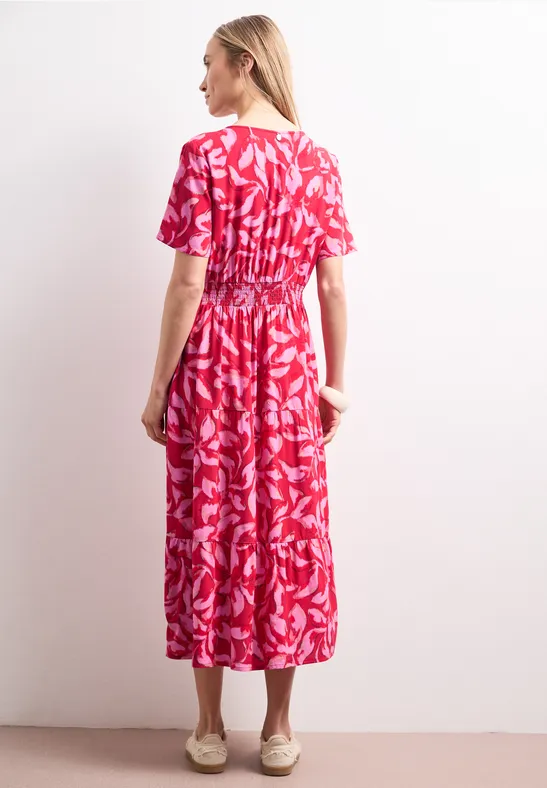 Frau von hinten in knöchellangem, ausgestelltem Kleid mit roten, weißen Blattmustern.
