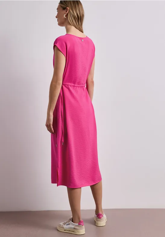 Vrouw van achteren in roze midijurk met korte mouwen en witte sneakers.