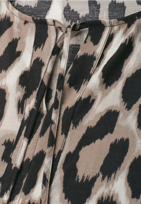 Close-up van een kledingstuk met beige luipaardprint en zwarte vlekken.