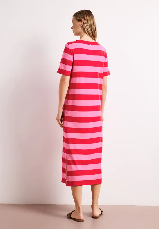 Eine Frau steht seitlich im gestreiften Midi-Kleid in Rot- und Pinktönen.