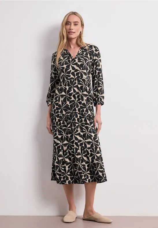 Vrouw in zwarte midijurk met beige sterprint, getailleerd model en beige instappers.