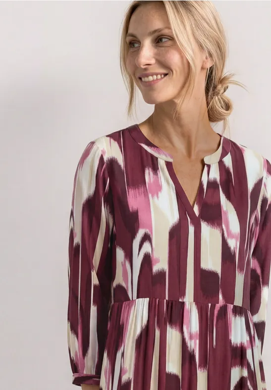 Vrouw in losse jurk met abstracte penseelstreekprint in paars en wit.