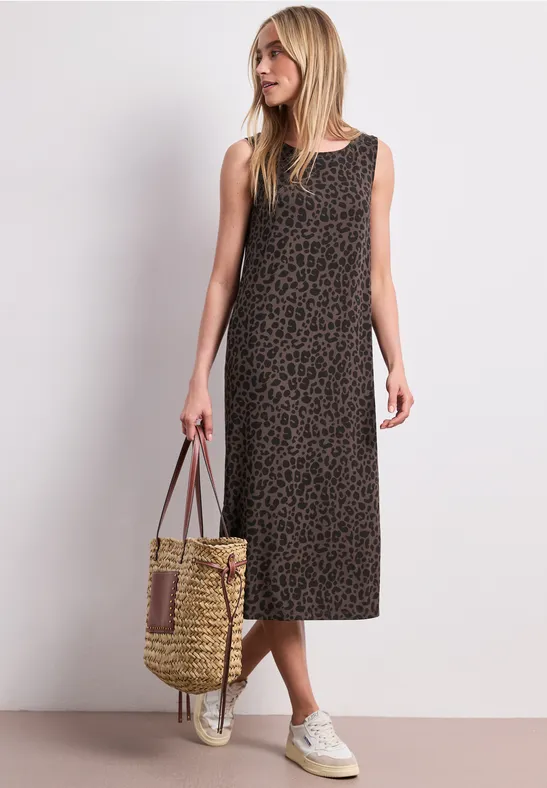 Femme en robe midi sans manches à imprimé léopard, baskets blanches et sac en paille tressée.