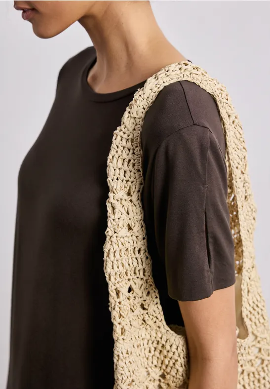 Persoon in donkerbruine T-shirt met een beige gehaakte tas over de schouder.