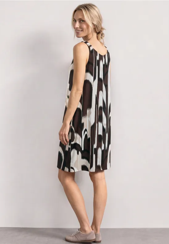 Femme de profil portant une robe ample sans manches à motifs abstraits noir et blanc, fond clair.