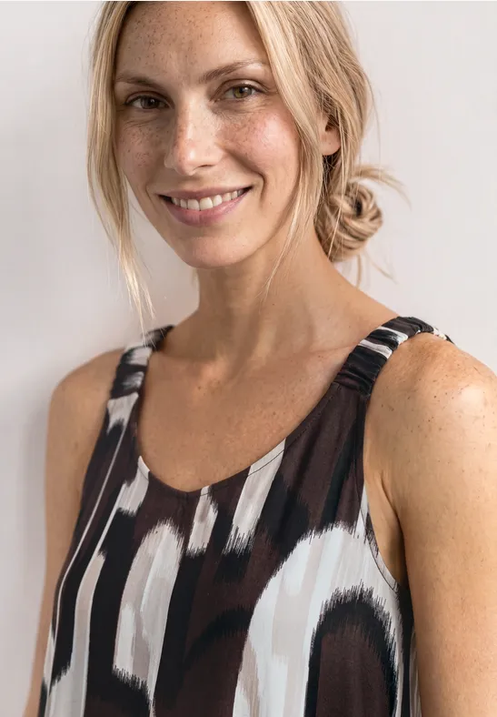 Femme aux cheveux attachés porte un top sans manches à motif abstrait noir et blanc sur fond clair.