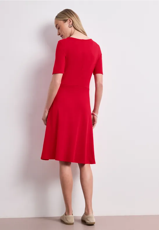 Een vrouw in een rood, knielang jurkje met driekwartmouwen, zijdelings vanaf achteren.