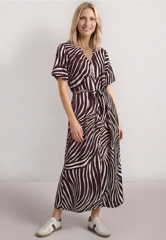 Vrouw in een midi-jurk met zebraprint, korte mouwen, tailleceintuur en witte sneakers.