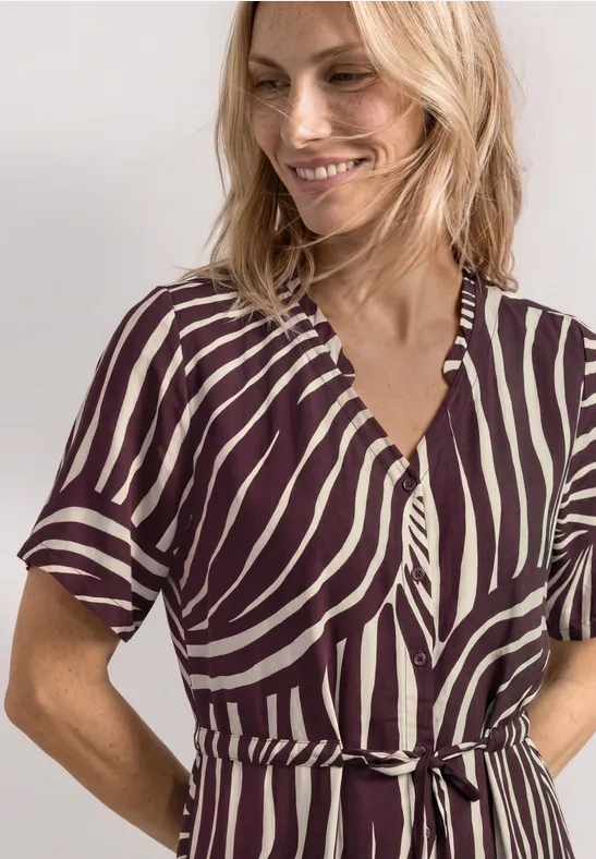 Een vrouw met een lichte glimlach draagt een getailleerde zebraprint jurk met korte mouwen en ceintuur.