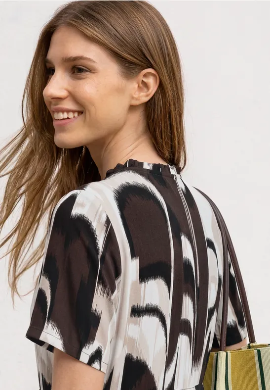Rugzicht van een model in een loszittende top met abstract zwart-wit-bruin dessin.