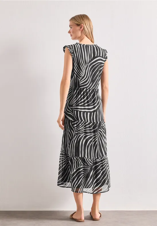 Vrouw in zwart-wit zebra midi-jurk, van achteren schuin gefotografeerd voor een lichte achtergrond.