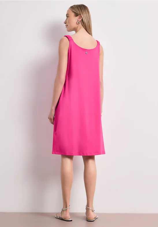 Vrouw in mouwloze roze jurk, rugaanzicht, met platte sandalen.