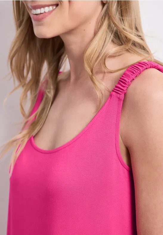 Zijaanzicht van een lachende vrouw in een felroze mouwloze top.