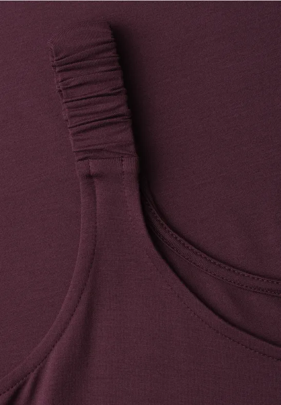 Close-up van een mouwloze bordeauxrode top met gerimpelde band.