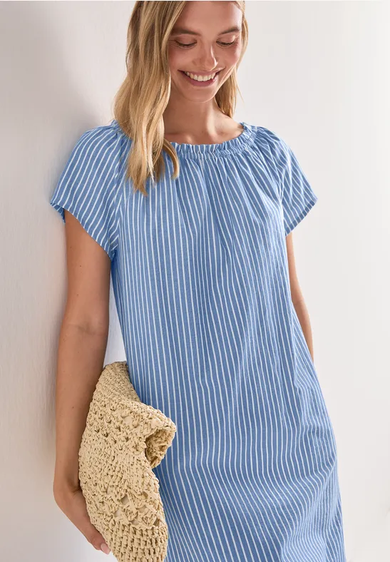 Een lachende vrouw in blauw-wit gestreepte jurk met gehaakte stro clutch.