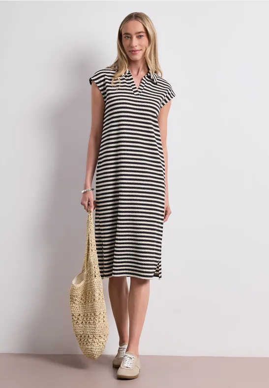 Vrouw in zwart-wit gestreepte midi-jurk met V-hals, draagt netzak en sneakers.