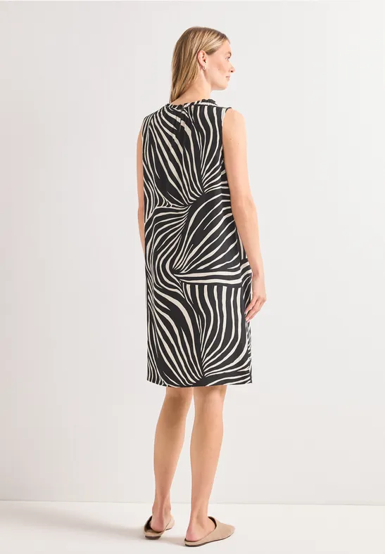 Vrouw van achteren in een knielange jurk met abstracte zwart-witte print en sandalen.